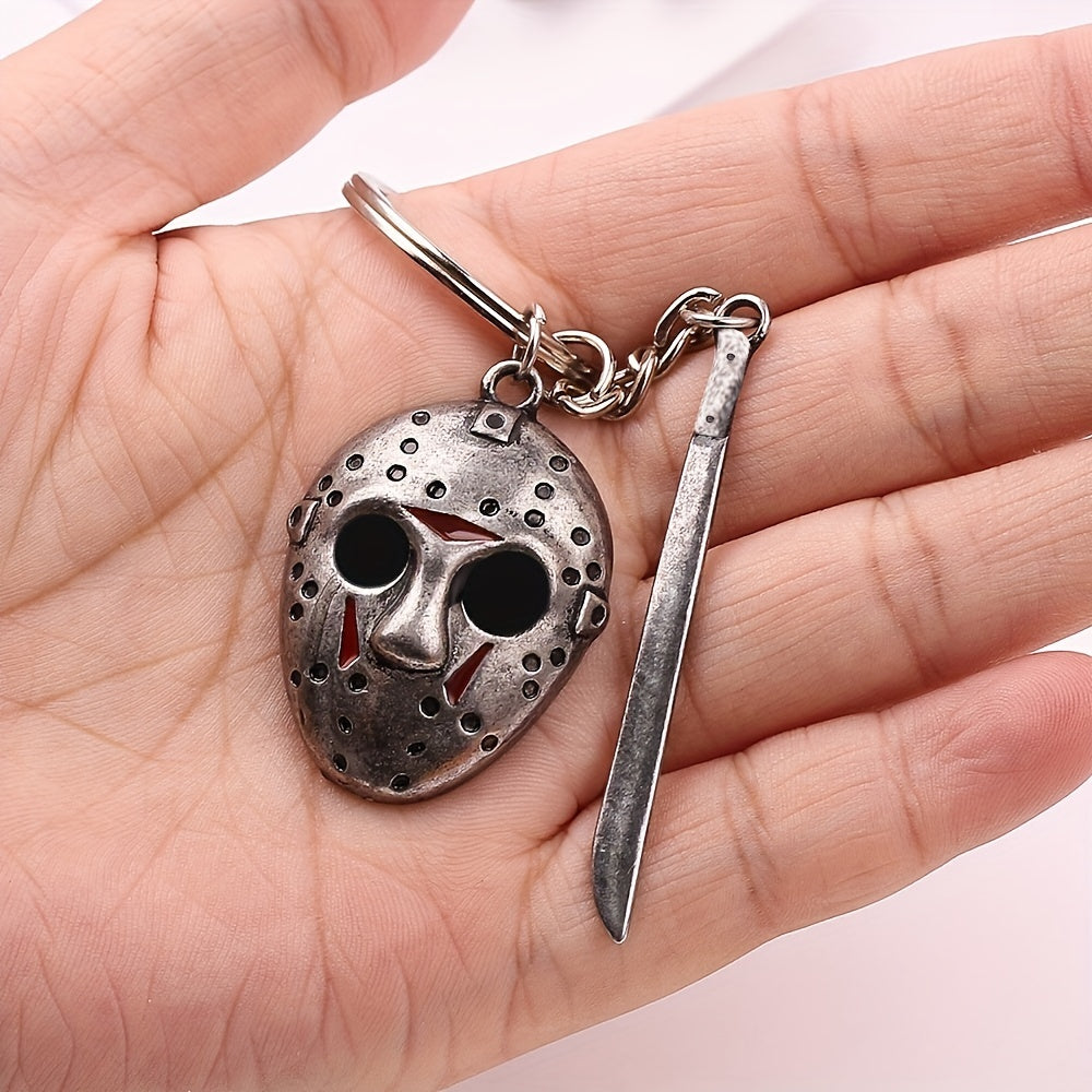 Metallic keychain with hockey mask and knife design held in a hand against a light background