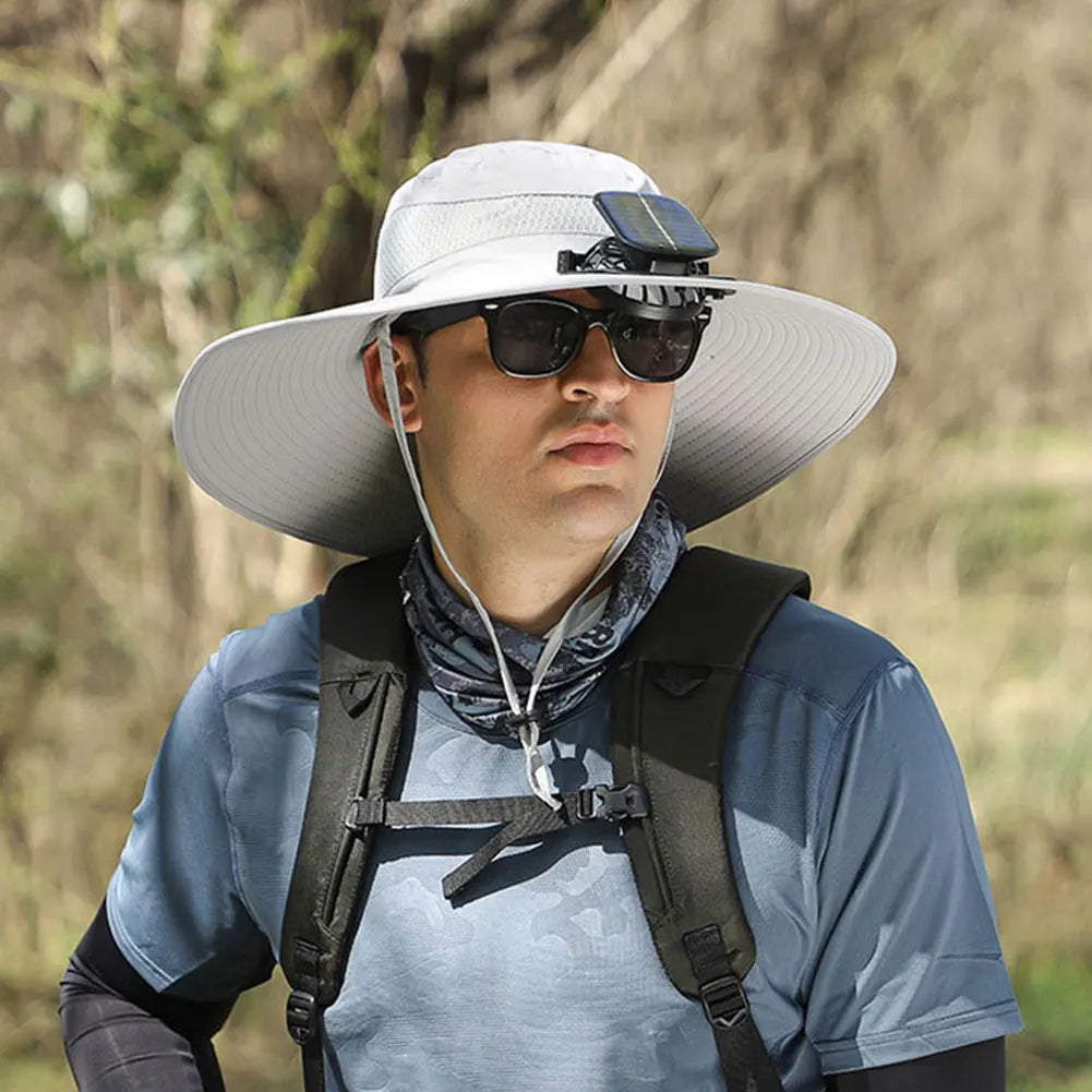 Person wearing a wide-brimmed hat with a solar panel, sunglasses, and a backpack in a natural setting.