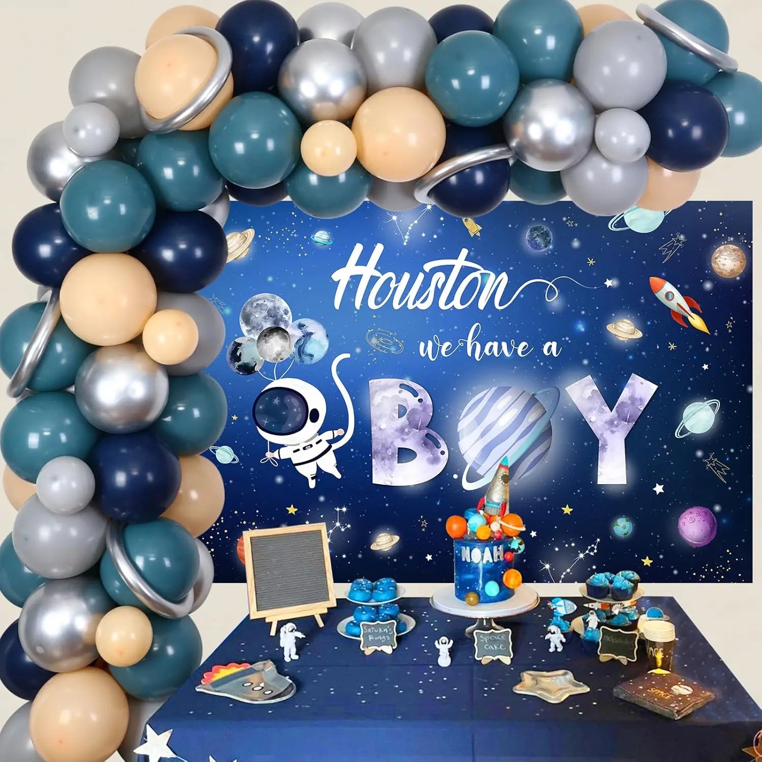 Space-themed baby shower setup with balloon arch, 'Houston we have a boy' backdrop, and space-themed decorations.