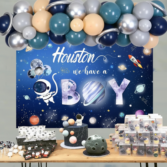 Space-themed baby shower setup with balloons, cake, and decorations against a 'Houston we have a boy' backdrop.