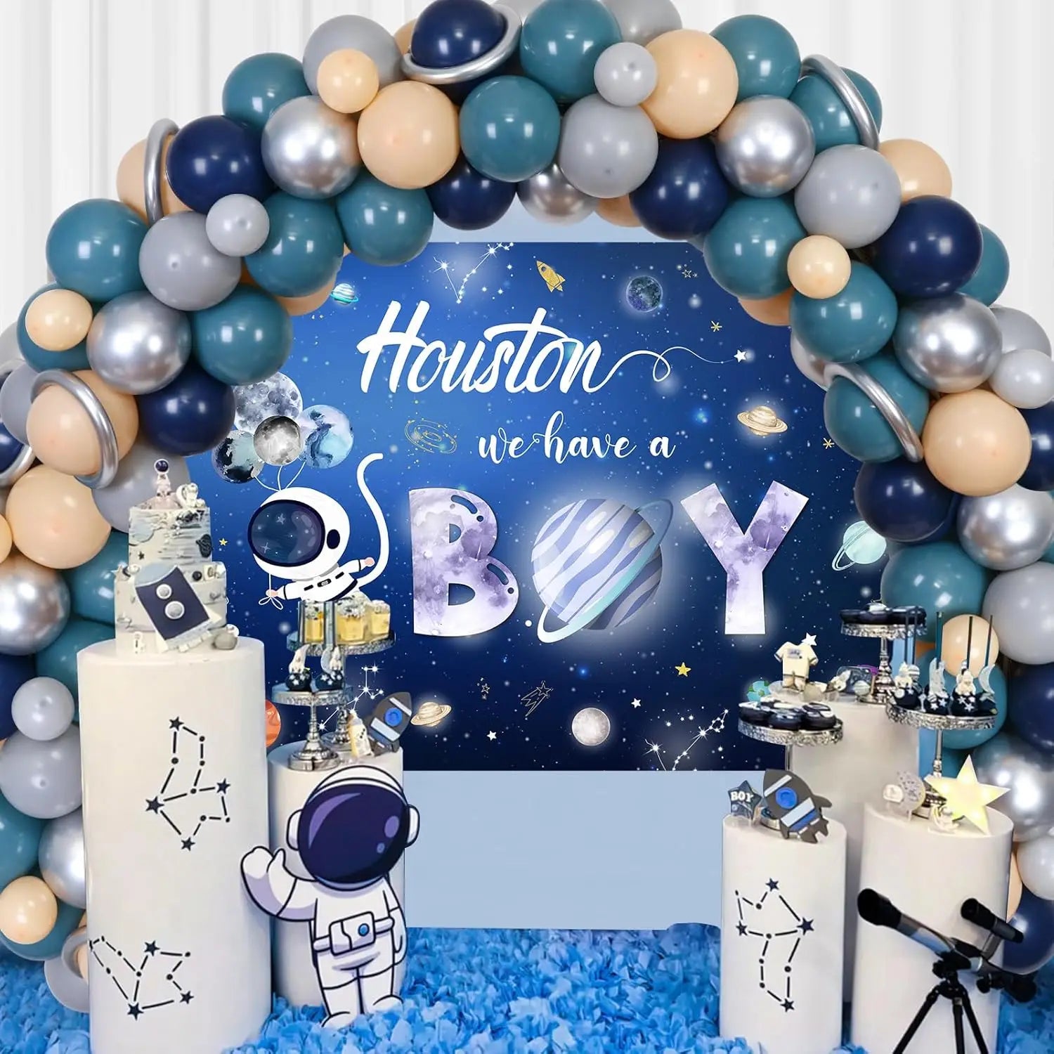 Space-themed baby shower decoration with balloons, astronaut figurines, and 'Houston we have a boy' sign.