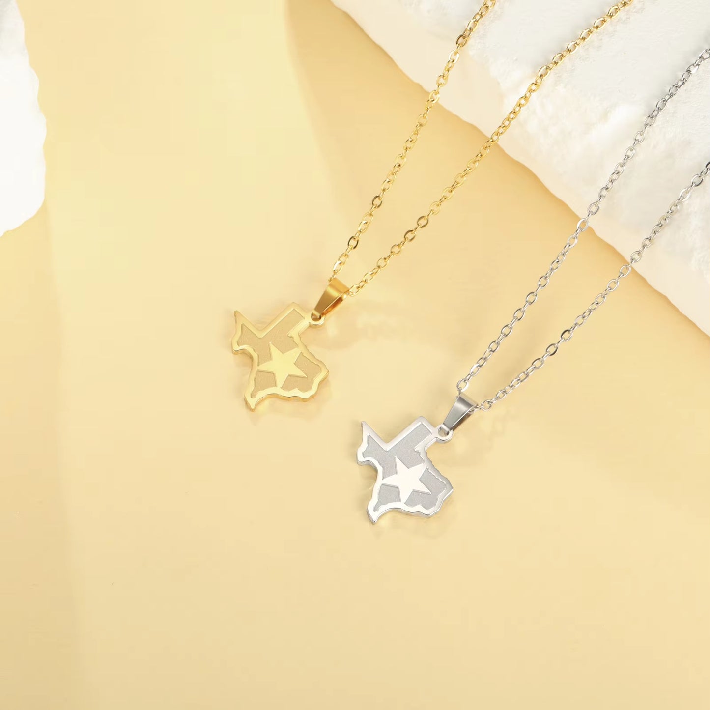 Two state of Texas necklaces in gold and silver, featured side-by-side and laid flat for full display of Texas pendant color options and link chain.