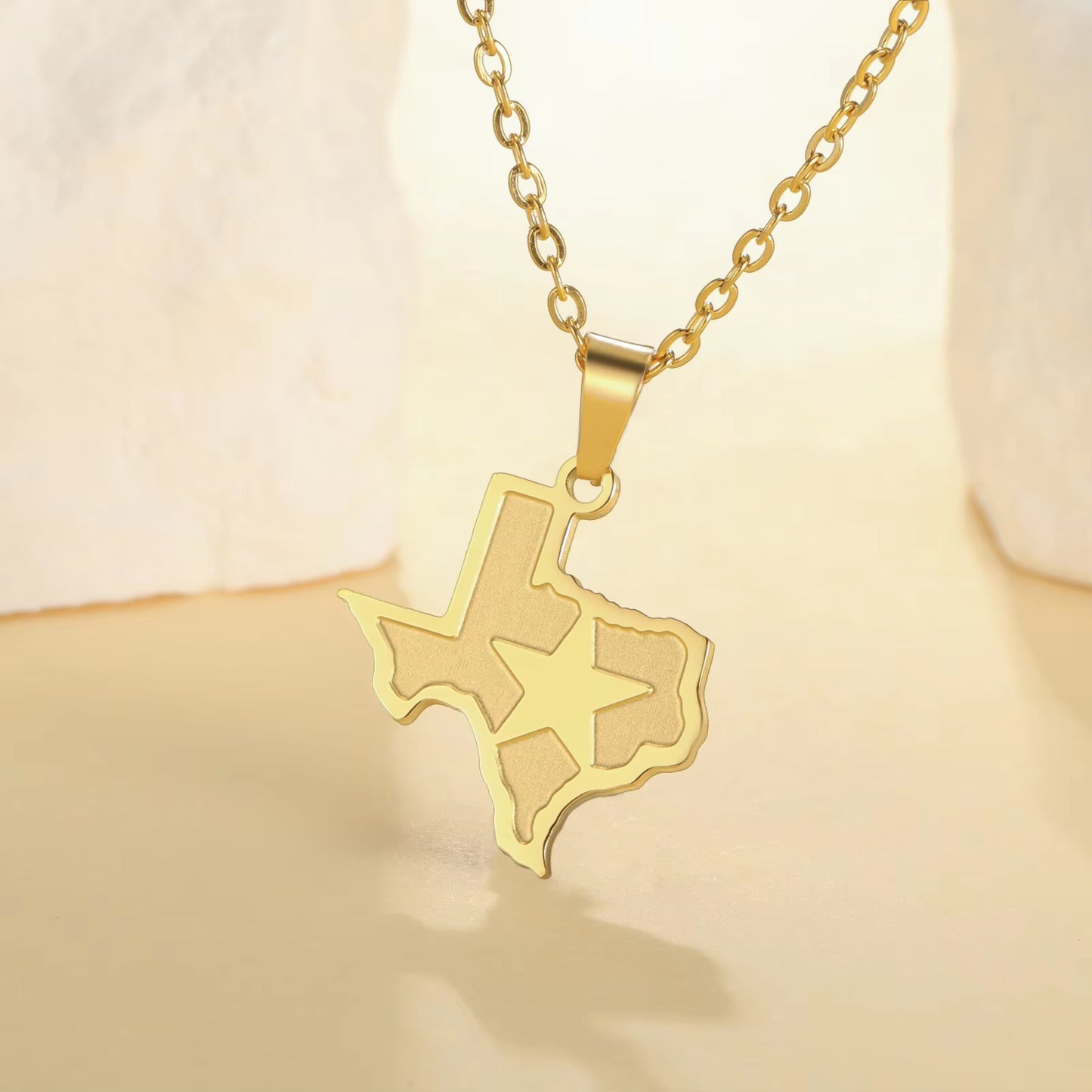 State of Texas necklace pendant with lone star over Texas and link chain in gold, featured draped over a stand on display and bright background.