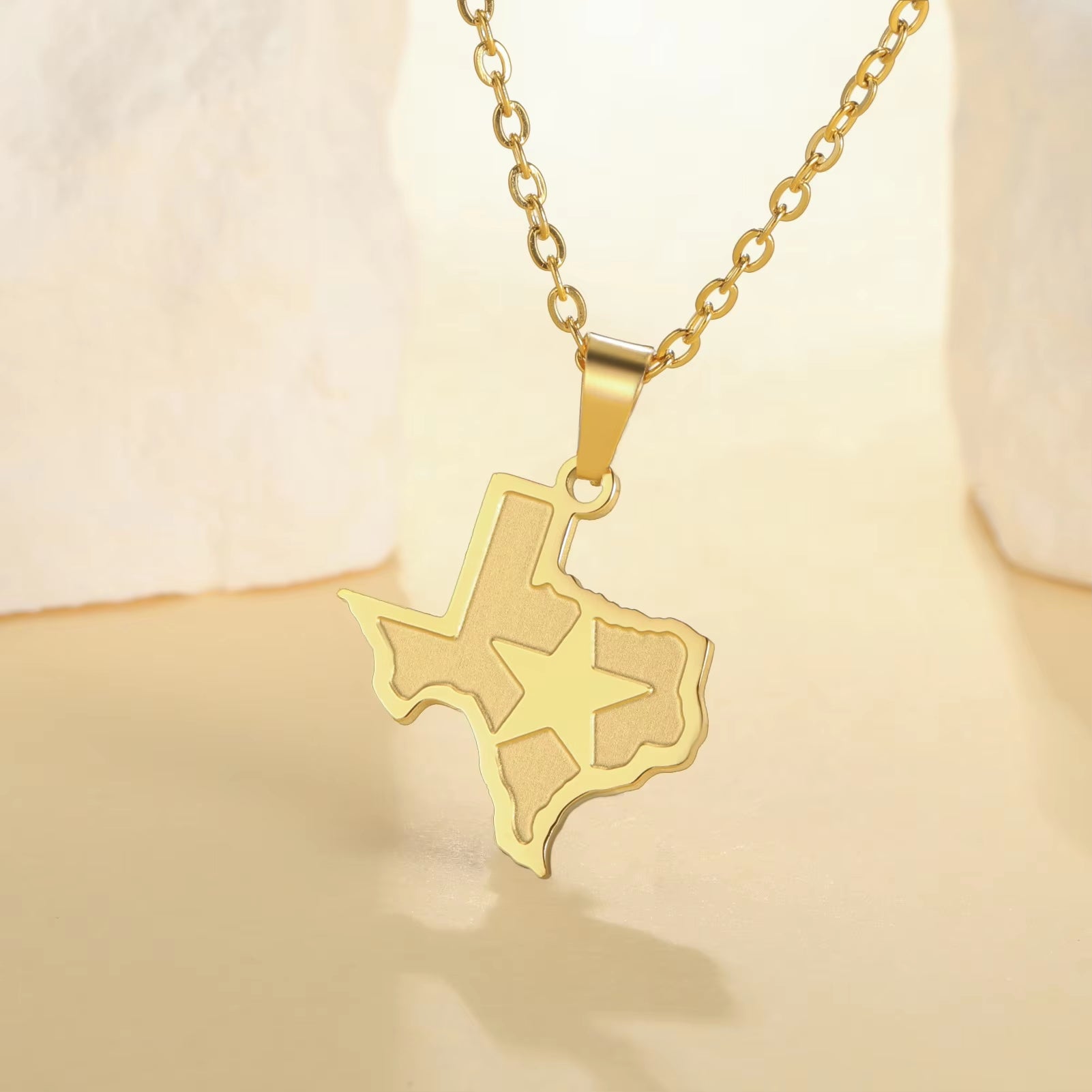 State of Texas necklace pendant with lone star over Texas and link chain in gold, featured draped over a stand on display and bright background.