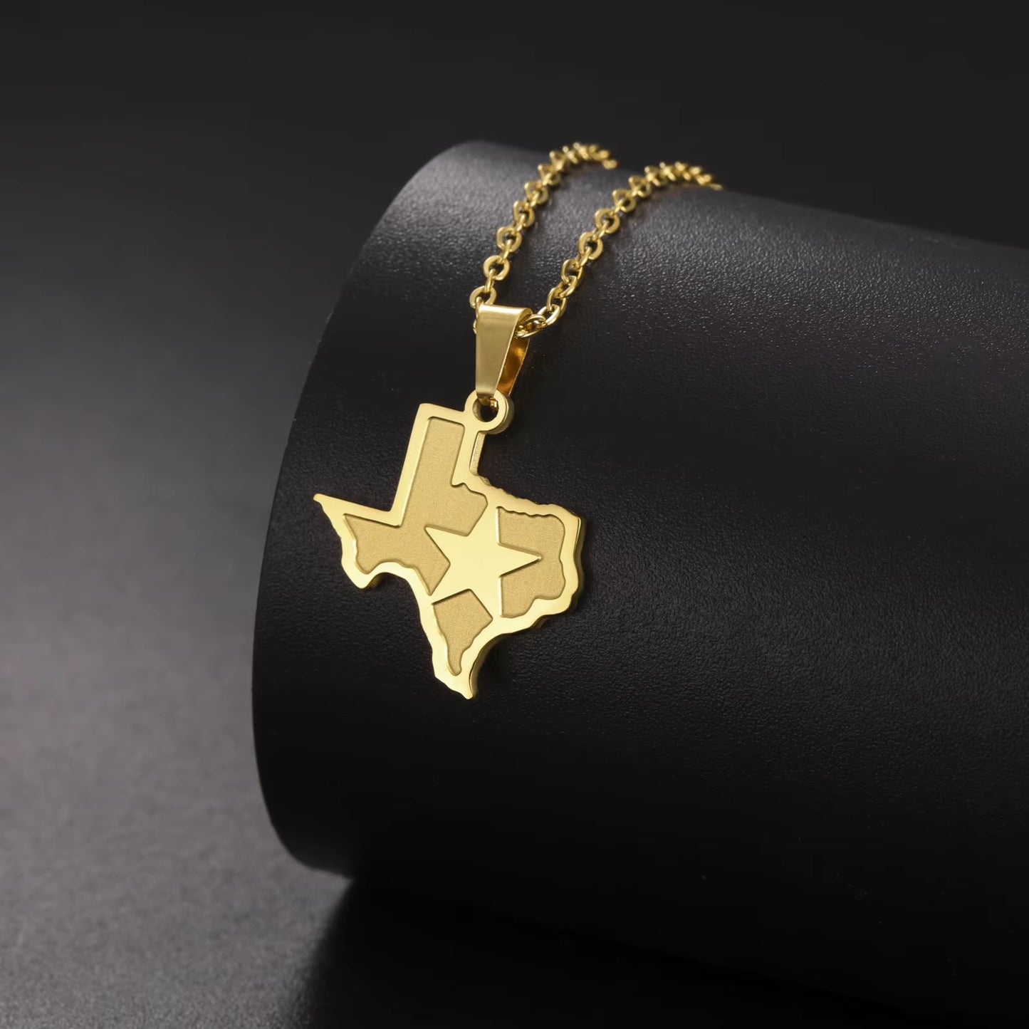 Gold Texas necklace with lone star pendant draped over a black display, with black background.