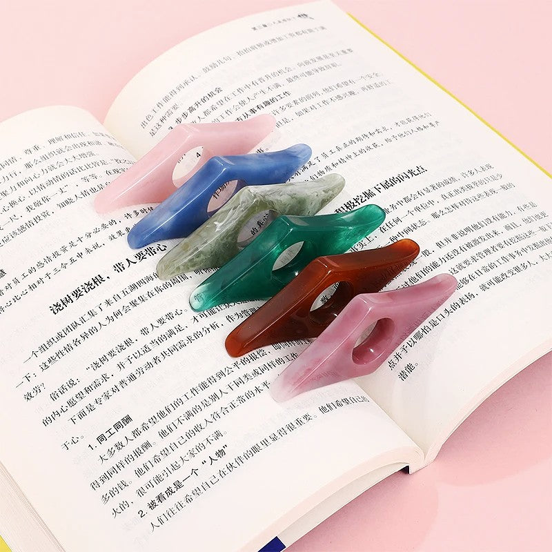 Collection of resin thumb bookmark page holders in assorted marbled colors (pink, blue, green, amber) resting on an open book.