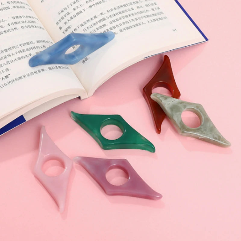 Collection of resin thumb bookmark page holders in assorted marbled colors (pink, blue, green, amber) resting on an open book.