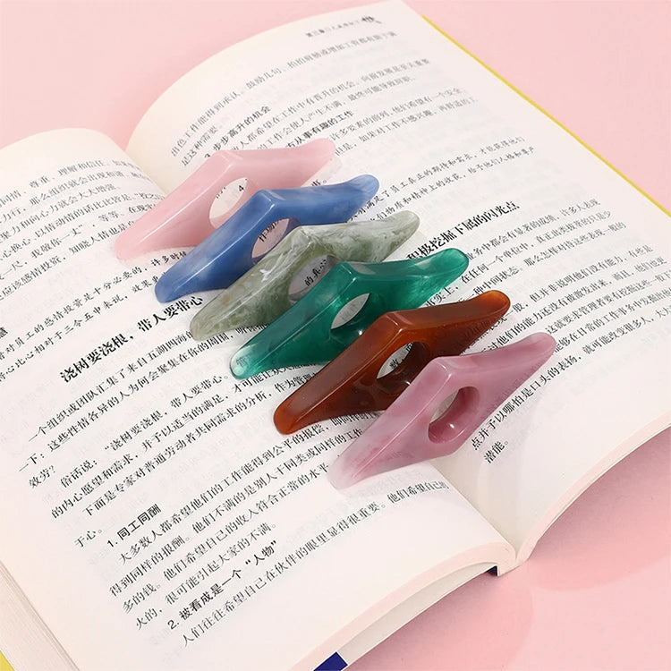 Collection of resin thumb bookmark page holders in assorted marbled colors (pink, blue, green, amber) resting on an open book.