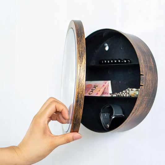 Wooden wall-mounted safe with a hand opening the cover to reveal money inside.
