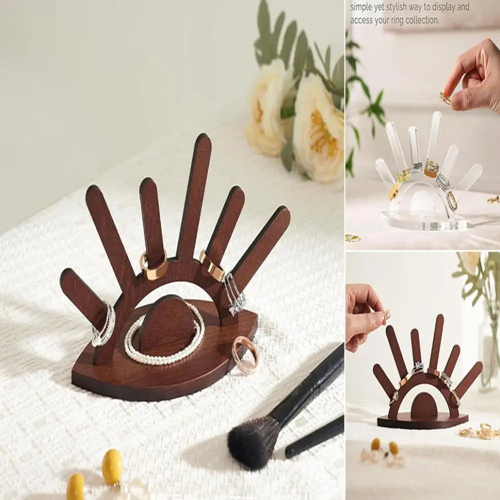 Wooden hand-shaped ring holder with rings displayed on a white surface.