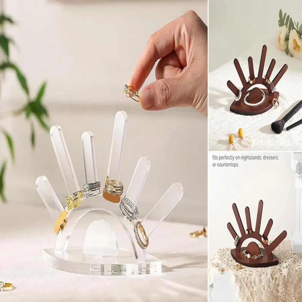 Clear acrylic ring holder with rings on a white surface, next to decorative hand-shaped stands.