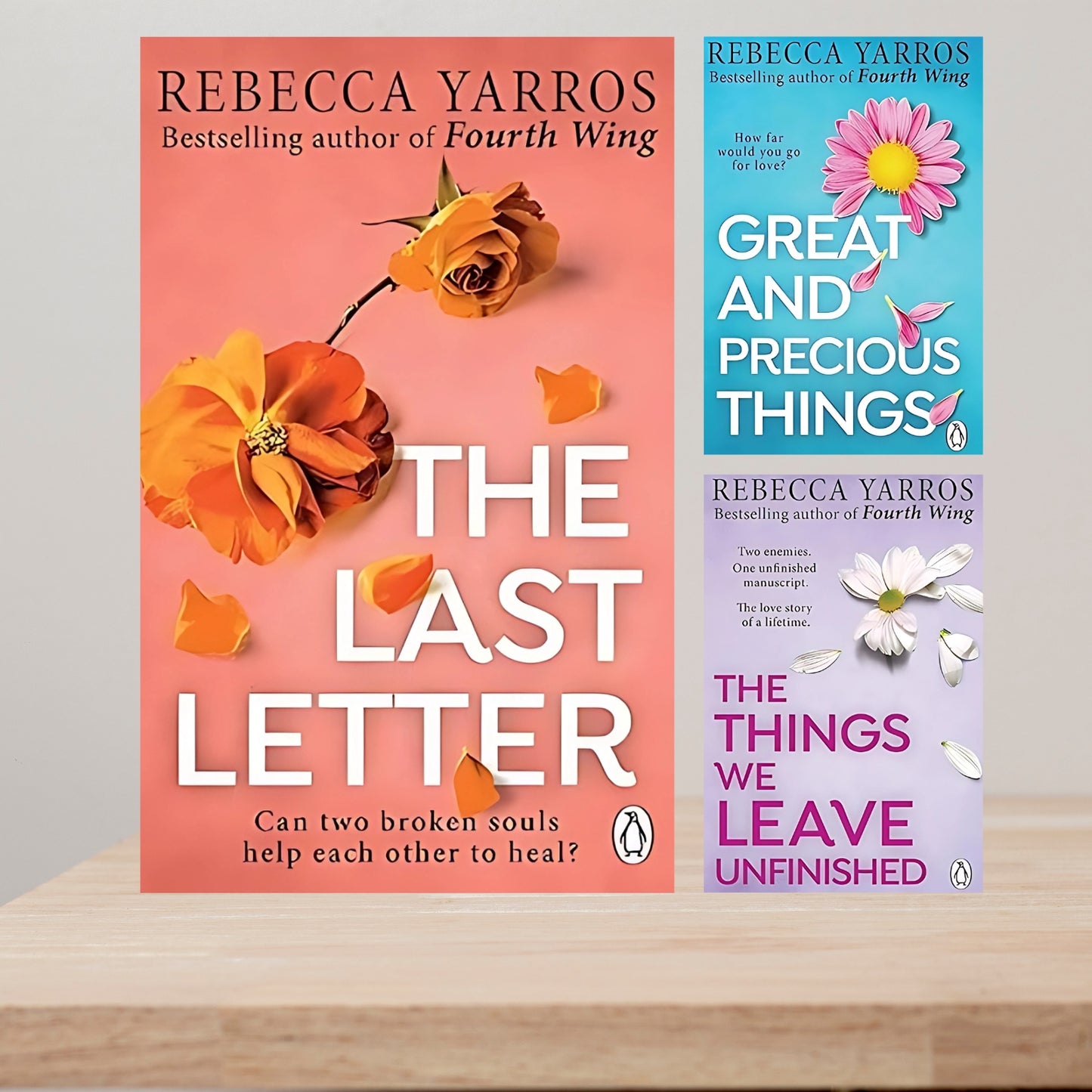 Three book covers by Rebecca Yarros on a wooden surface with a gray background