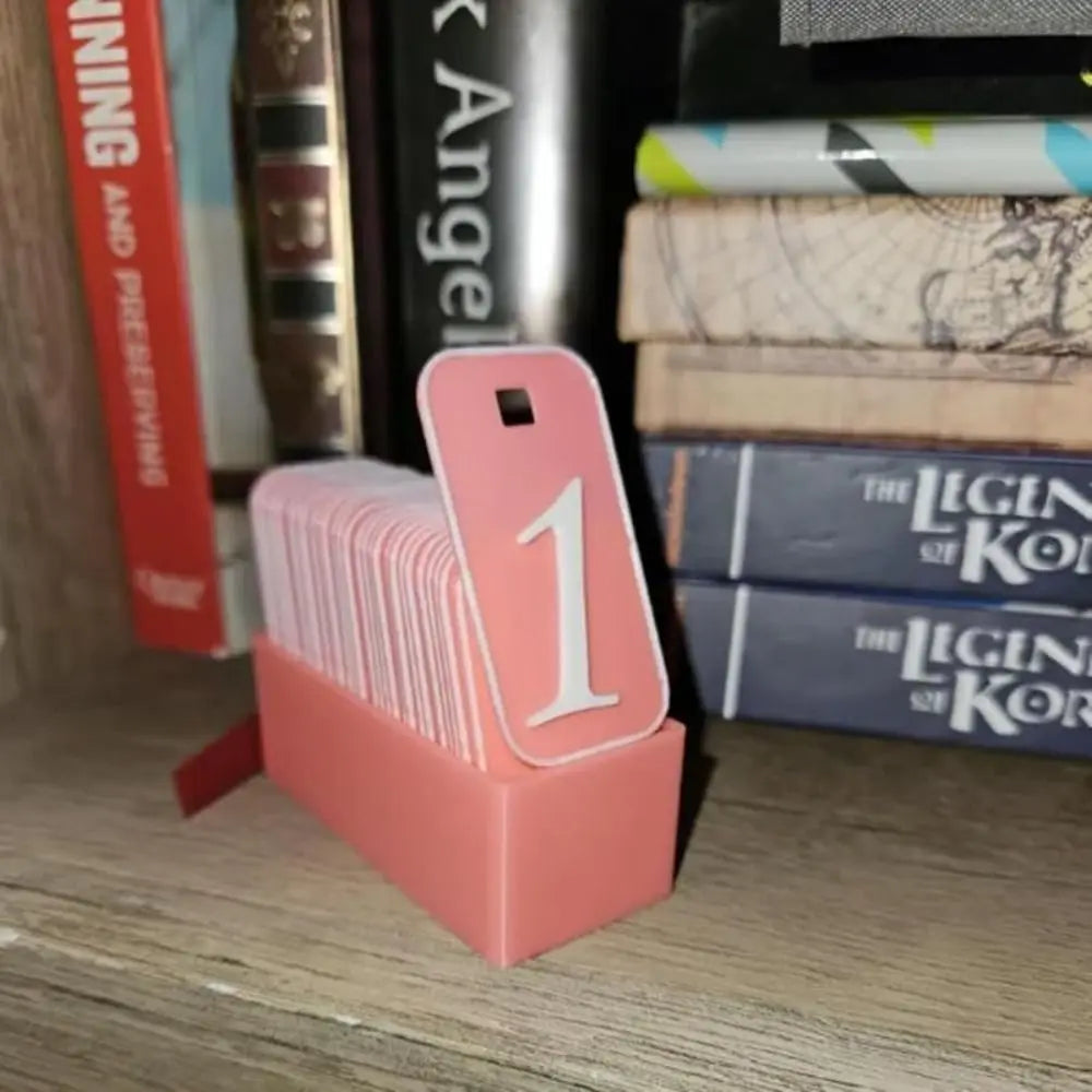 Pink card holder numbers for books read tracker bookshelf accessory with number '1' in front of books on a wooden surface.